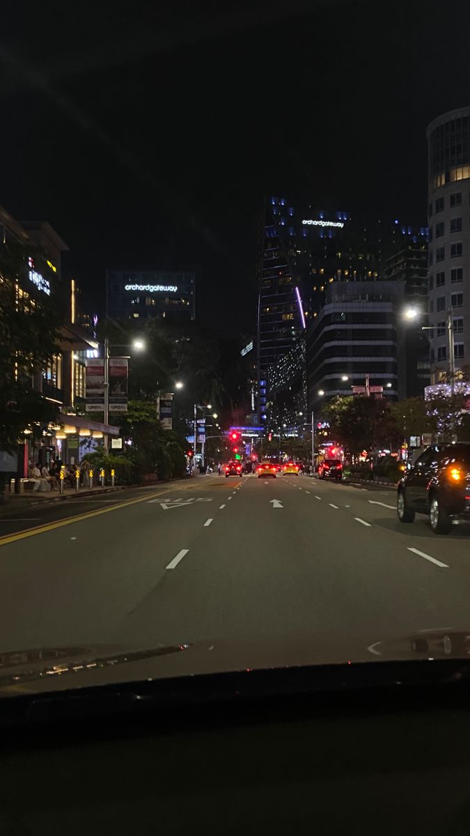 a city street at night with cars driving down it's sides and tall buildings in the background