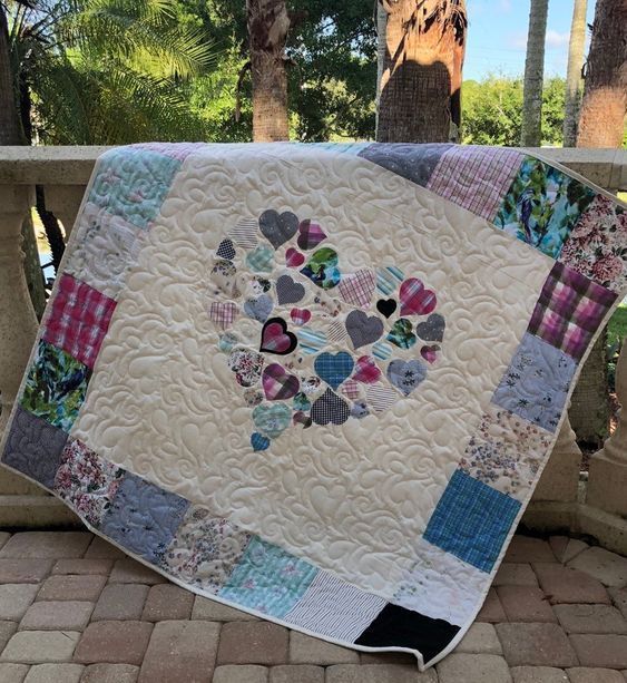 a quilted heart is displayed on a stone wall next to trees and palm trees