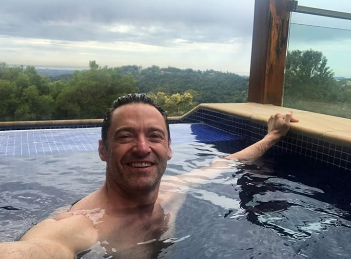 a man in a hot tub smiling at the camera with his arm out and head above water