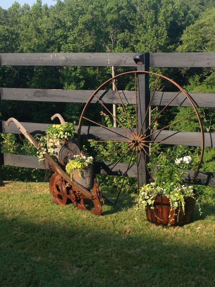 an old fashioned wheel and some plants in pots on the grass near a fenced in area