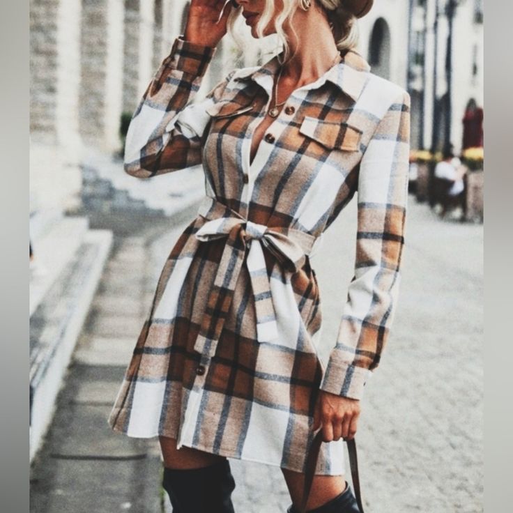 a woman is standing on the sidewalk talking on her cell phone while wearing boots and a plaid shirt dress