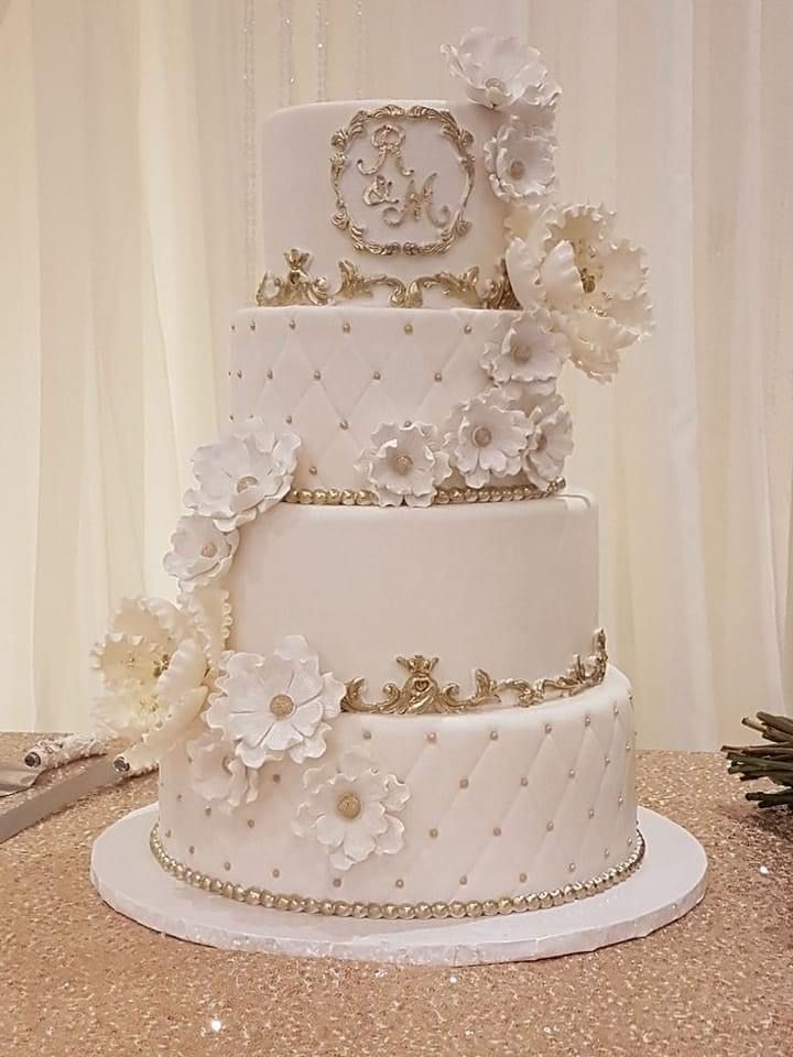 a three tiered wedding cake with white flowers on the top and gold trimmings