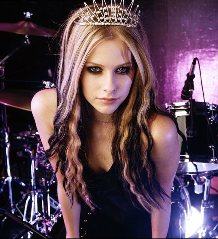 a woman with long hair wearing a tiara and posing in front of drum set