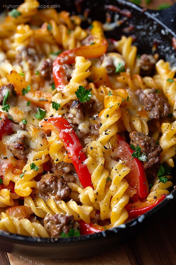 a skillet filled with pasta, meat and vegetables on top of a wooden table