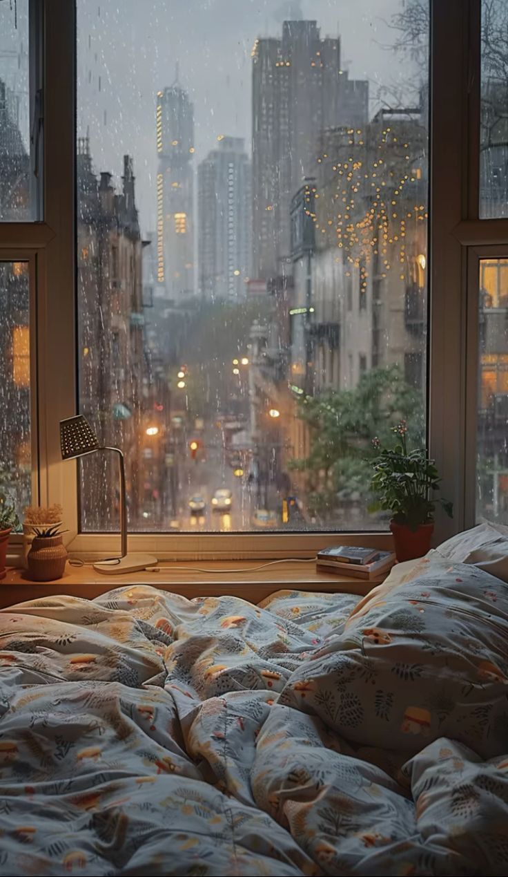 a bed sitting in front of a window next to a night time cityscape