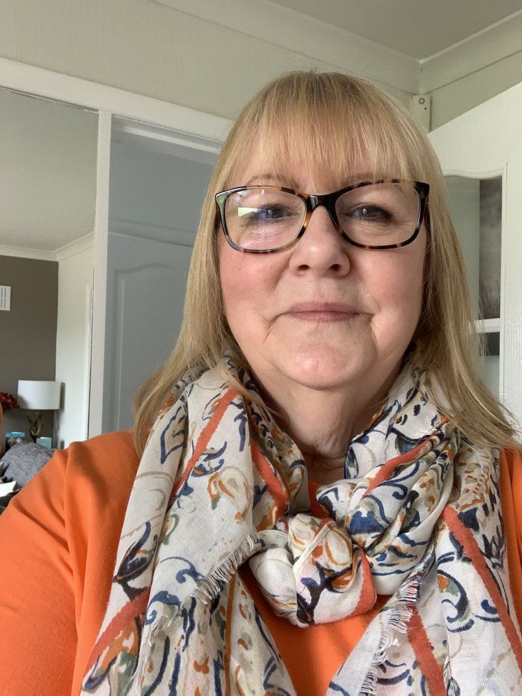 a woman wearing glasses and an orange shirt is smiling at the camera with her scarf around her neck