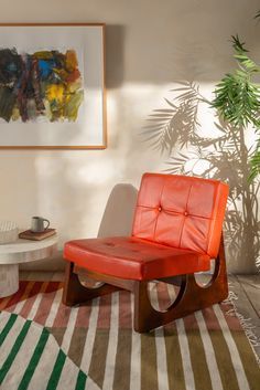 an orange chair sitting on top of a rug next to a table and potted plant