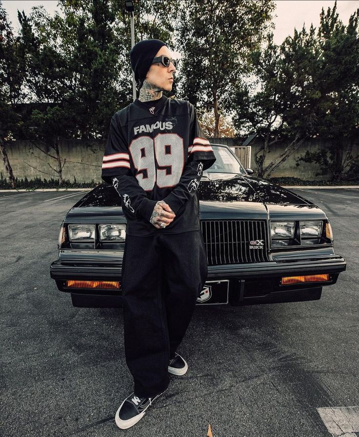 a man standing in front of a black car wearing a jersey and hat with the number 98 on it