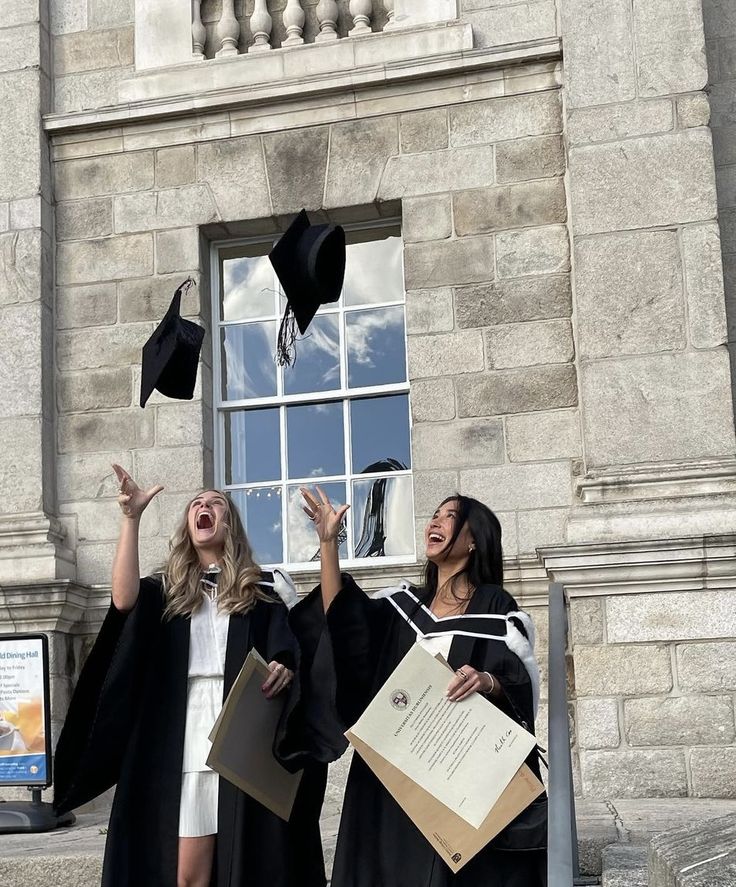 two women in graduation gowns throwing their caps into the air while one woman holds her hand up