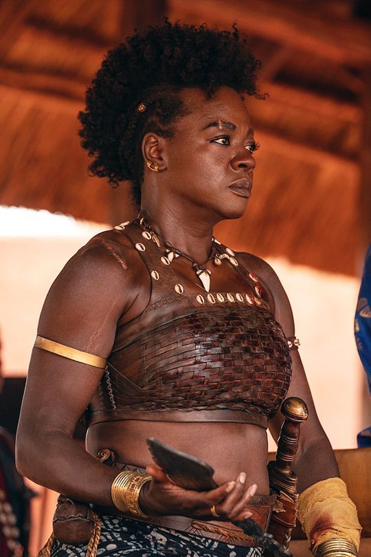 a woman in a brown top and gold bracelets holding a piece of paper while standing next to other people