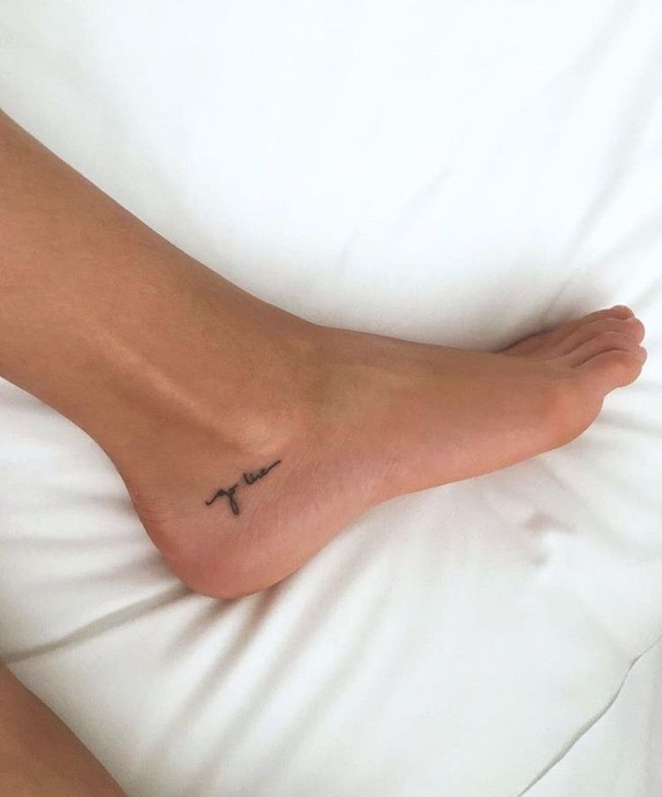 a person's foot with a cross tattoo on it sitting on a white bed