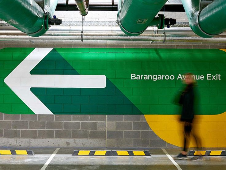 a man walking past a green and yellow sign in a parking garage with an arrow pointing to the left