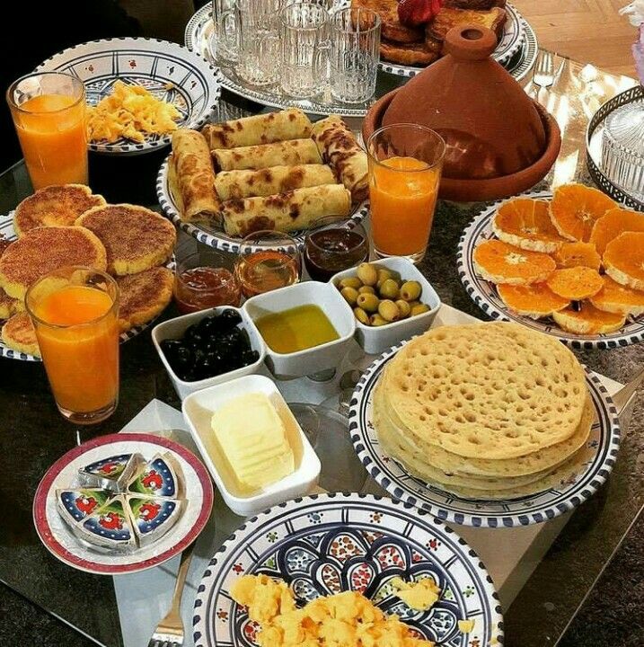 a table full of breakfast foods and oranges on plates, cups, and saucers