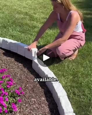 a woman kneeling down next to a flower bed