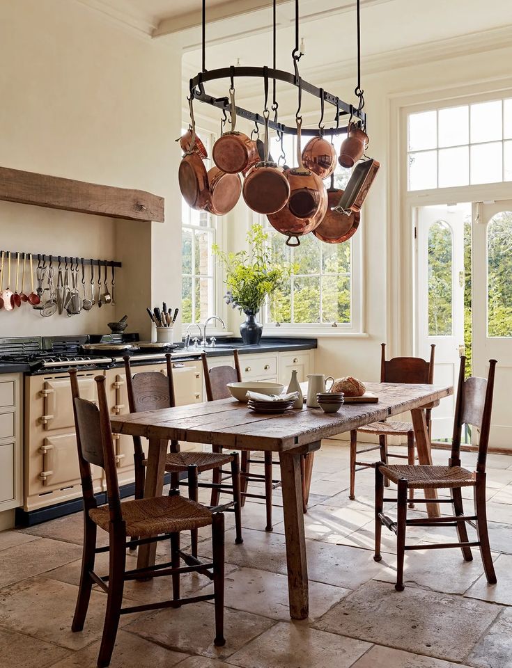 a dining room table and chairs with pots hanging from the ceiling