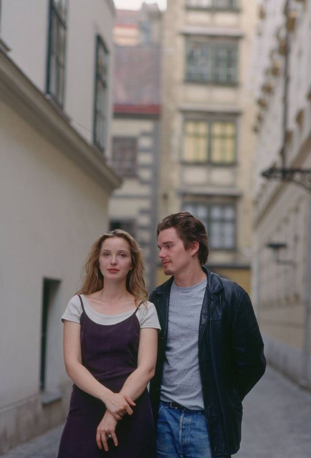 a man and woman standing in an alleyway next to each other with buildings behind them