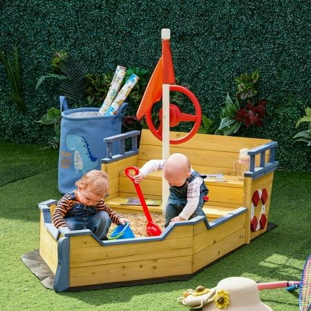 two toddlers playing in a wooden pirate ship play set on artificial grass with toys