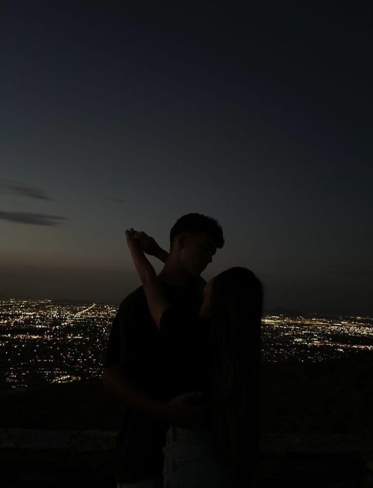 a man and woman standing next to each other in front of a city at night