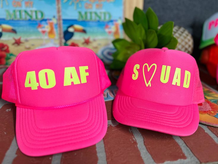 two pink hats with yellow letters on them sitting on a table next to other items