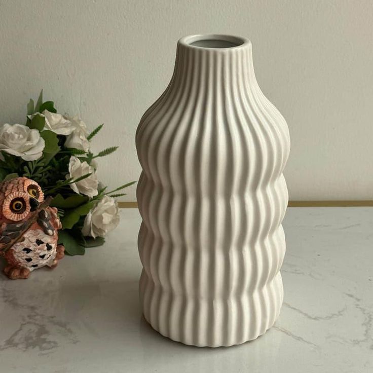 a white vase sitting on top of a table next to a flower pot and an owl figurine