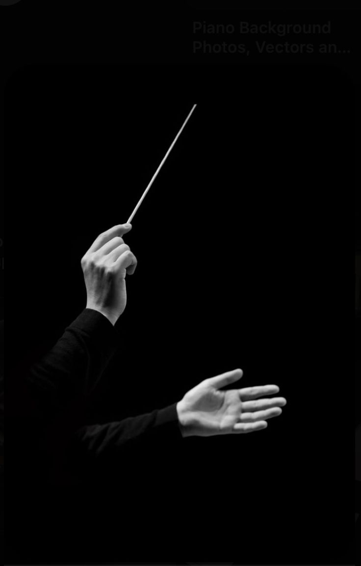 a person holding a conductor's baton in the dark with their hands extended out