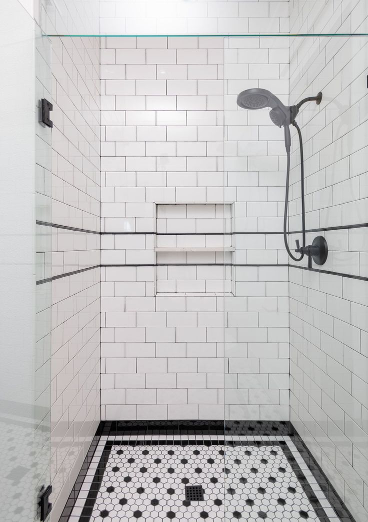 a white tiled shower with black and white floor tiles on the wall next to it