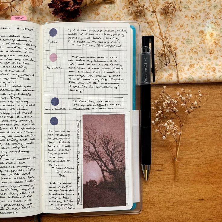 an open notebook sitting on top of a wooden table next to a pen and flowers