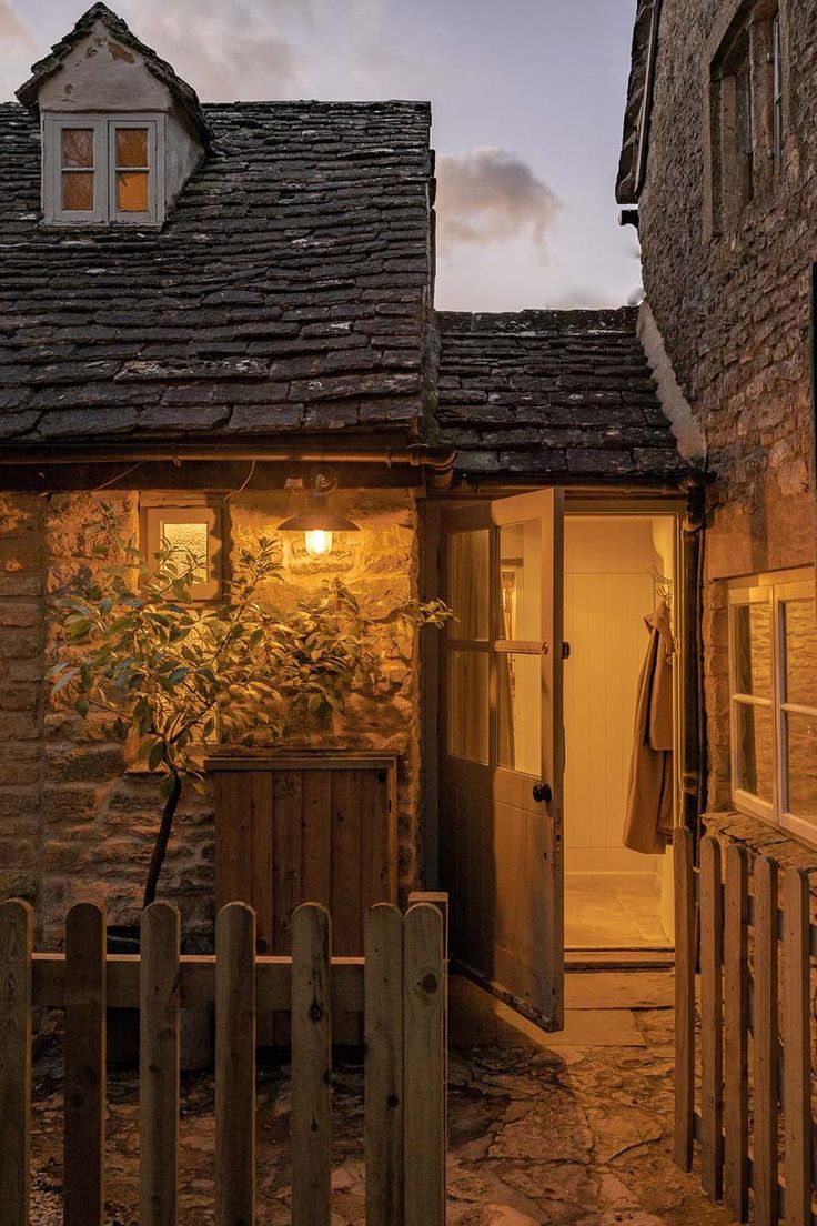 an old stone building with a door and window in the evening time, next to a wooden fence