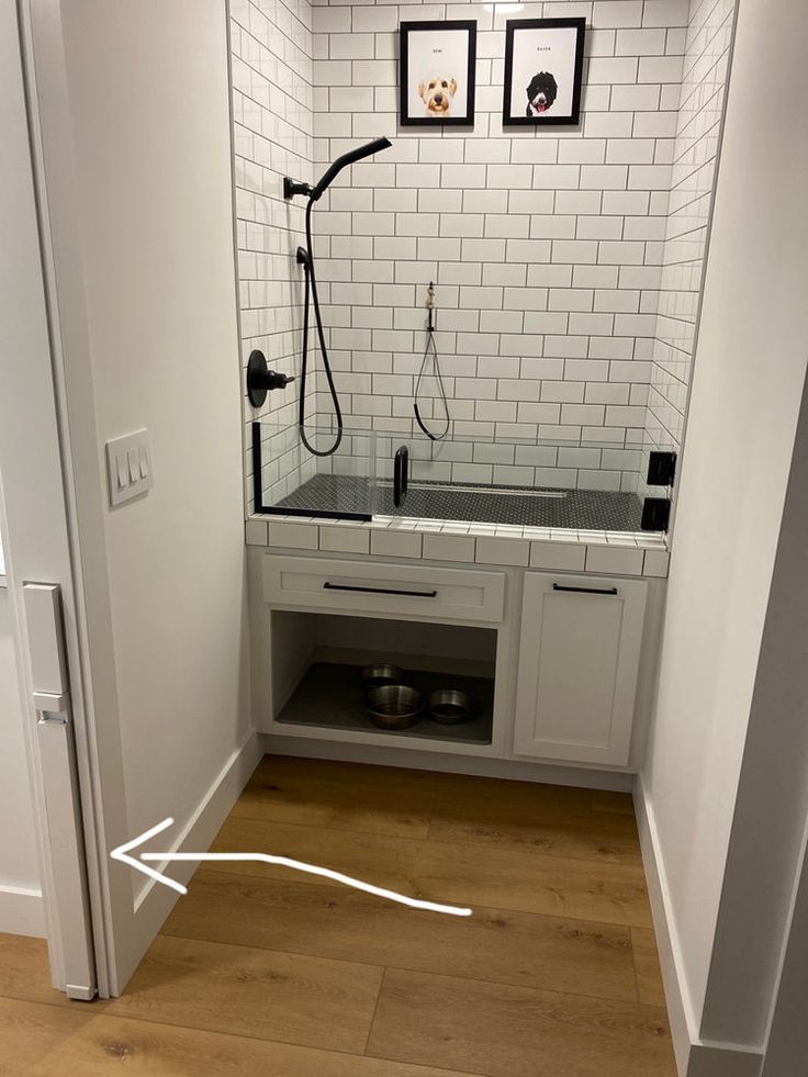 a bathroom with white tile walls and wooden flooring is shown in this image, there are two black faucets on the wall next to the sink