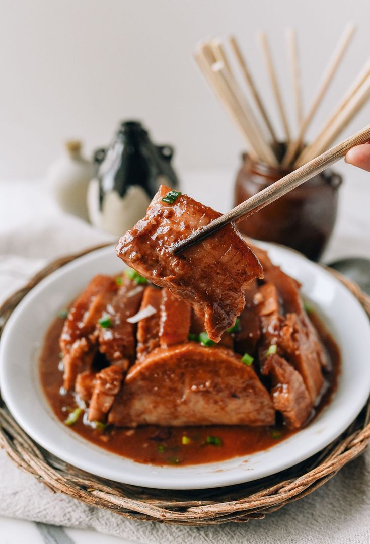 a person holding chopsticks over a plate of food with meat and sauce on it