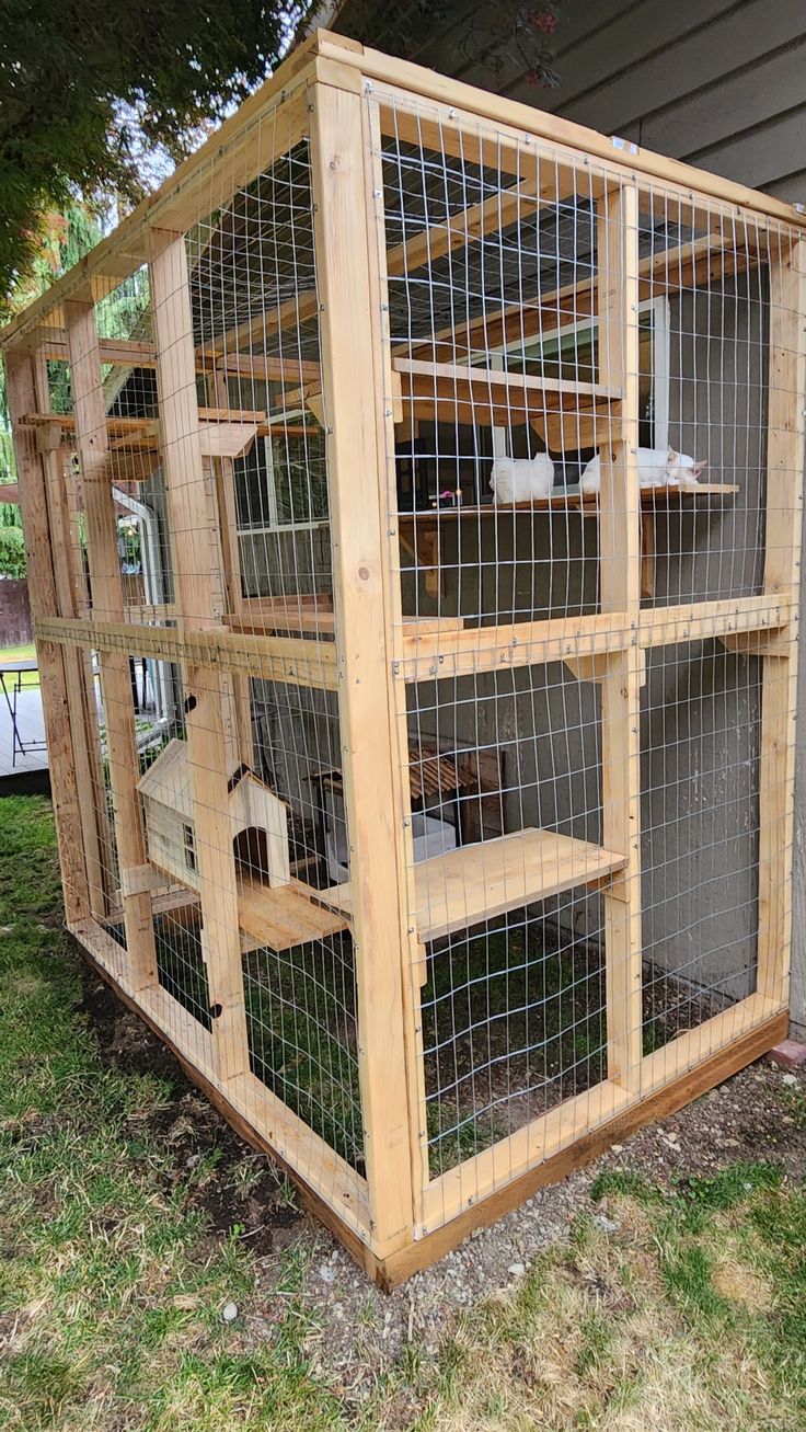 a large wooden cage with several cages in it on the grass next to a house