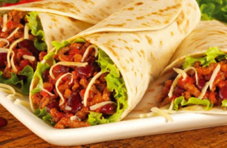 two burritos on a plate with lettuce and tomatoes