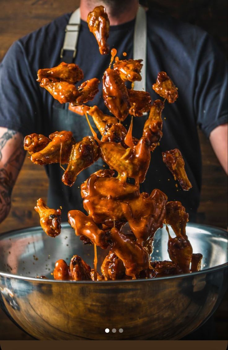 the man is pouring sauce on chicken wings