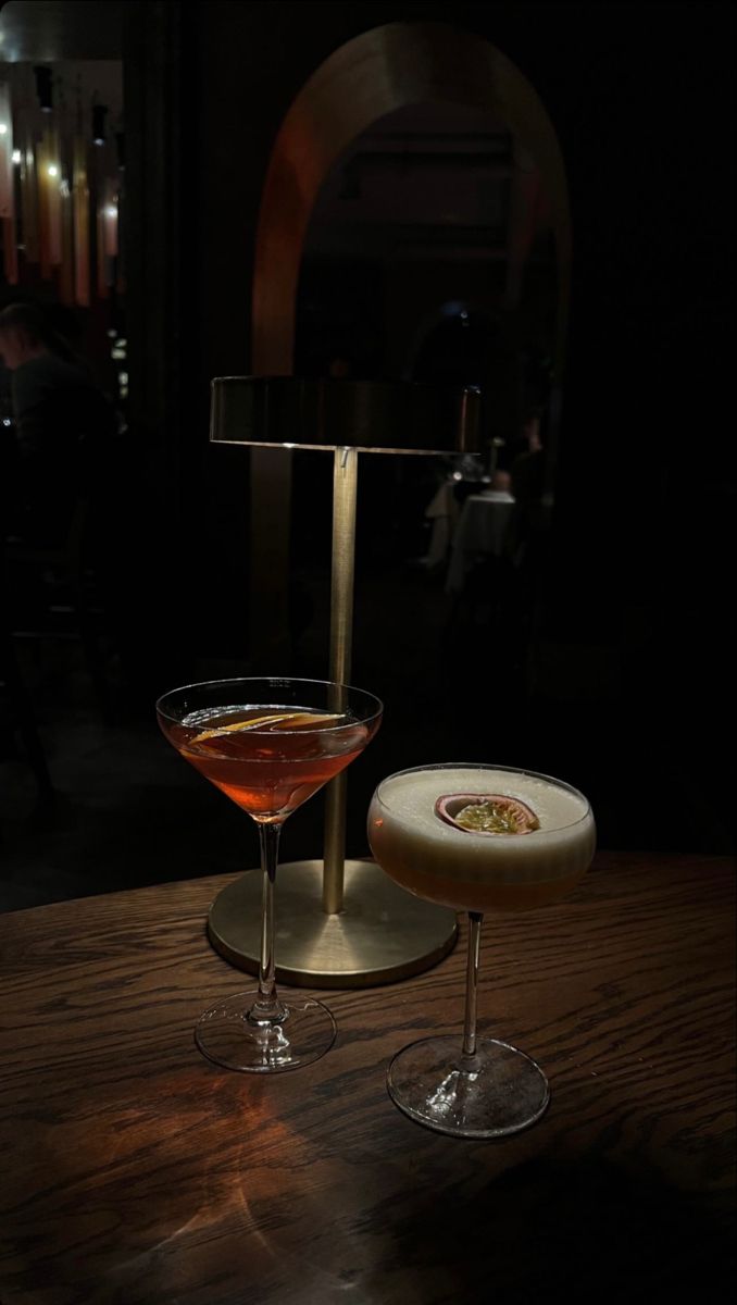 two martini glasses sitting on top of a wooden table next to a wine glass filled with liquid