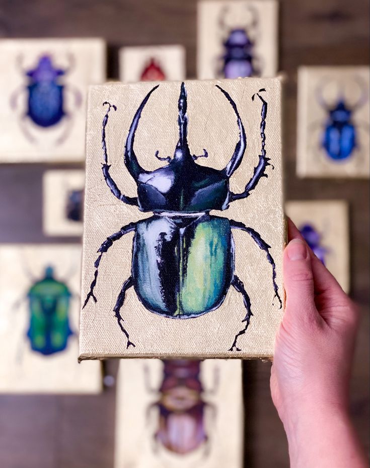 a hand holding up a small wooden block with a beetle painted on it