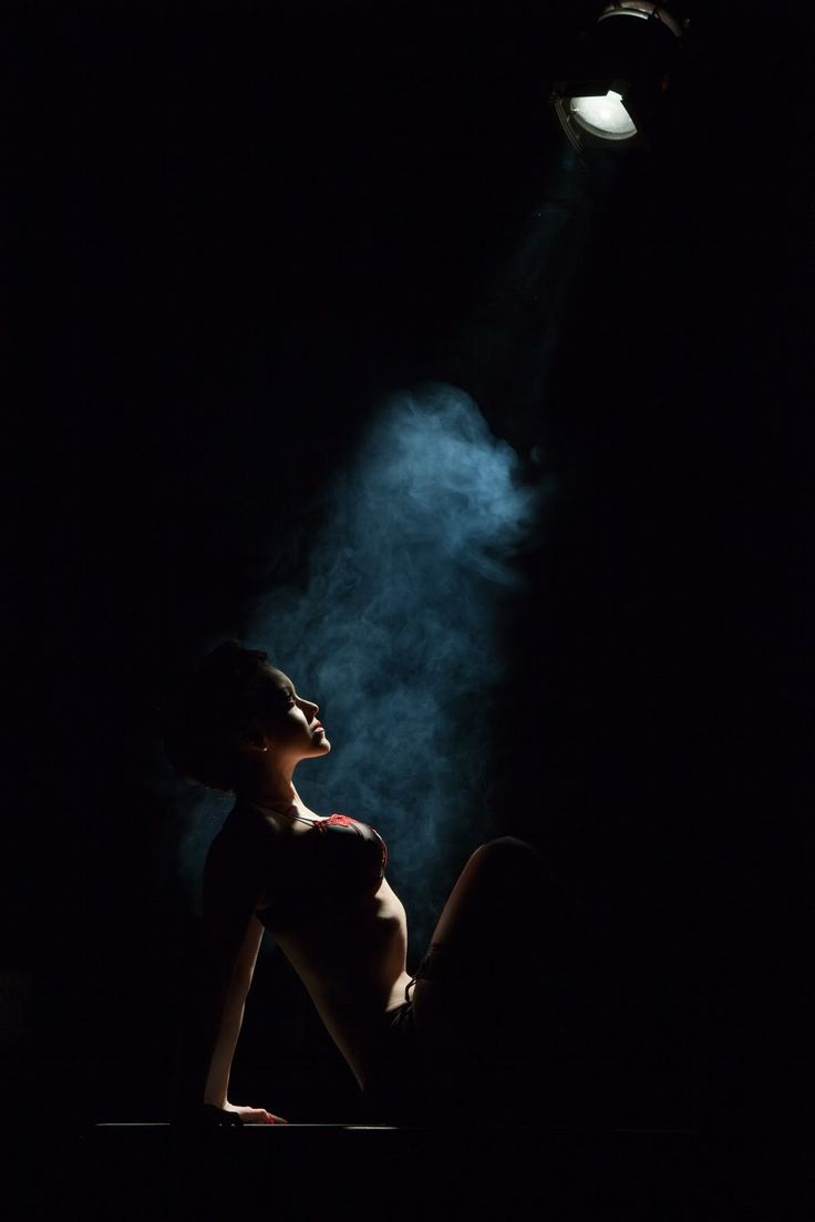 a woman is sitting in the dark with her head turned to the side and light shining on her