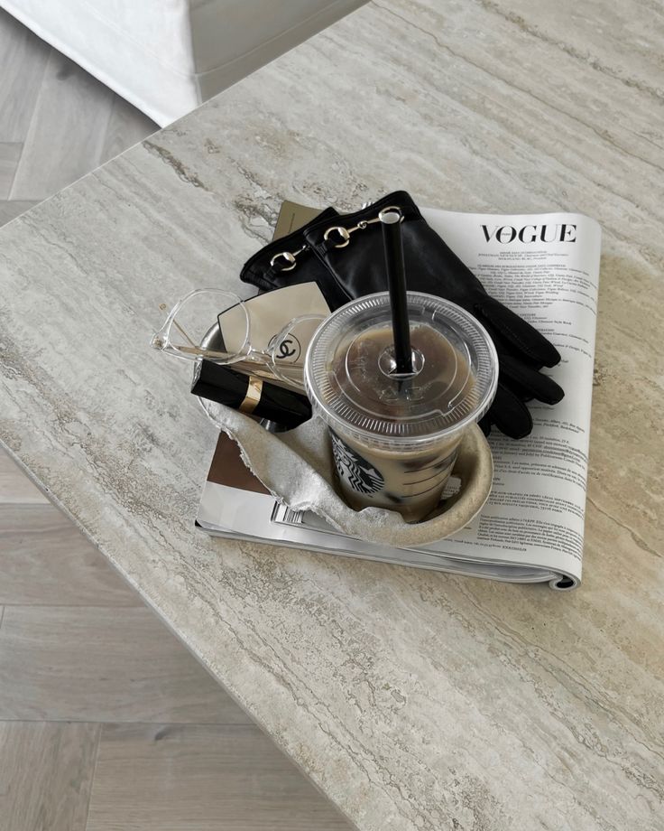 an open book on a table next to a pair of black gloves and a coffee cup