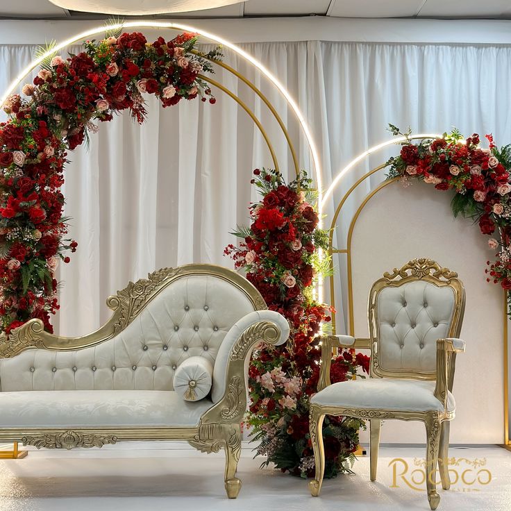 a white couch sitting next to a chair with flowers on the wall and an archway behind it