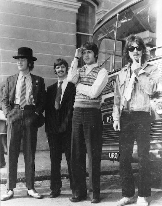 four young men standing next to each other in front of a bus, one holding his hat