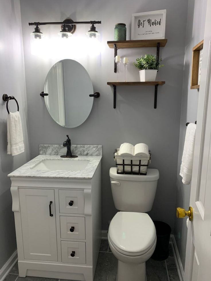 a white toilet sitting next to a sink in a bathroom under a mirror and shelves