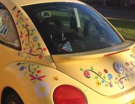 the back end of a yellow car with flowers painted on it's side window