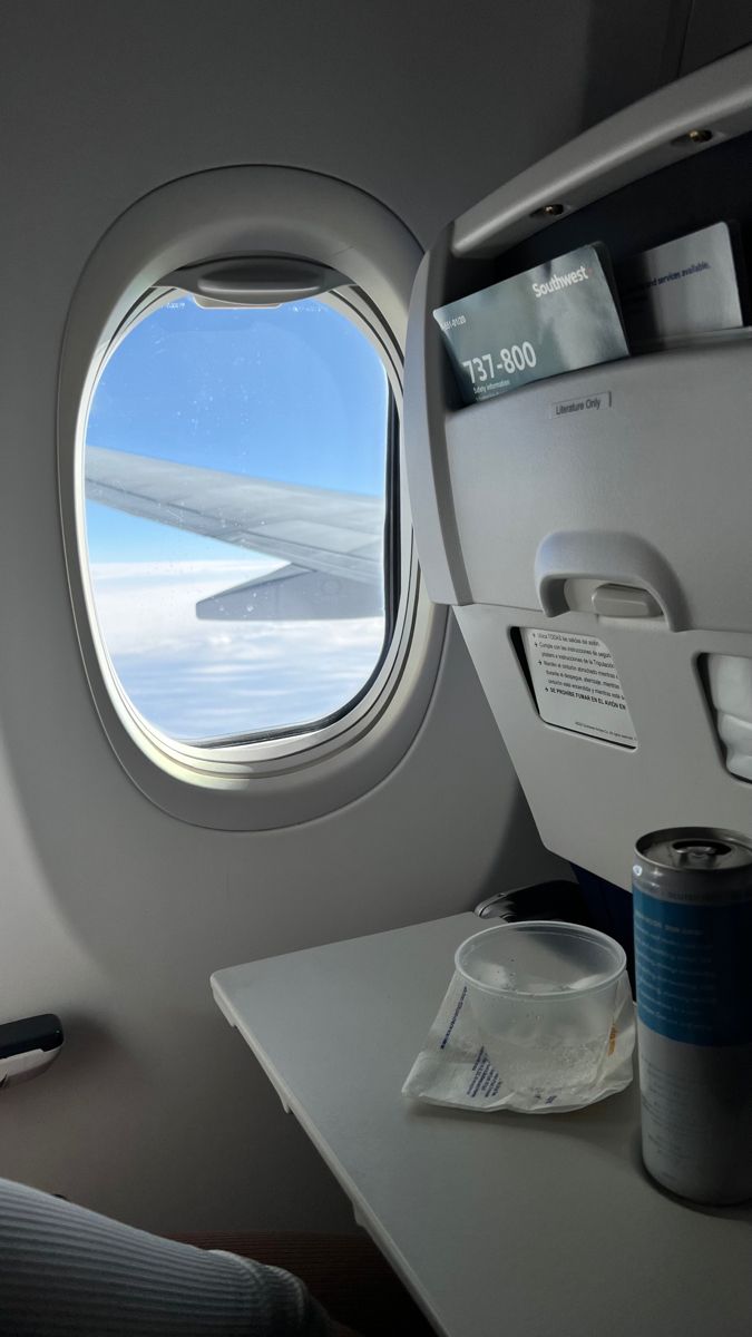 an airplane window looking out at the sky and clouds with a can of soda next to it