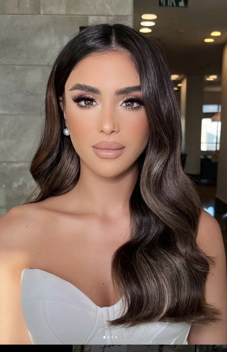 a woman with long brown hair wearing a strapless dress and diamond earrings, posing for the camera