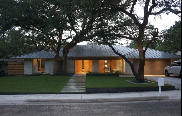 a house that is sitting on the side of a road with trees in front of it