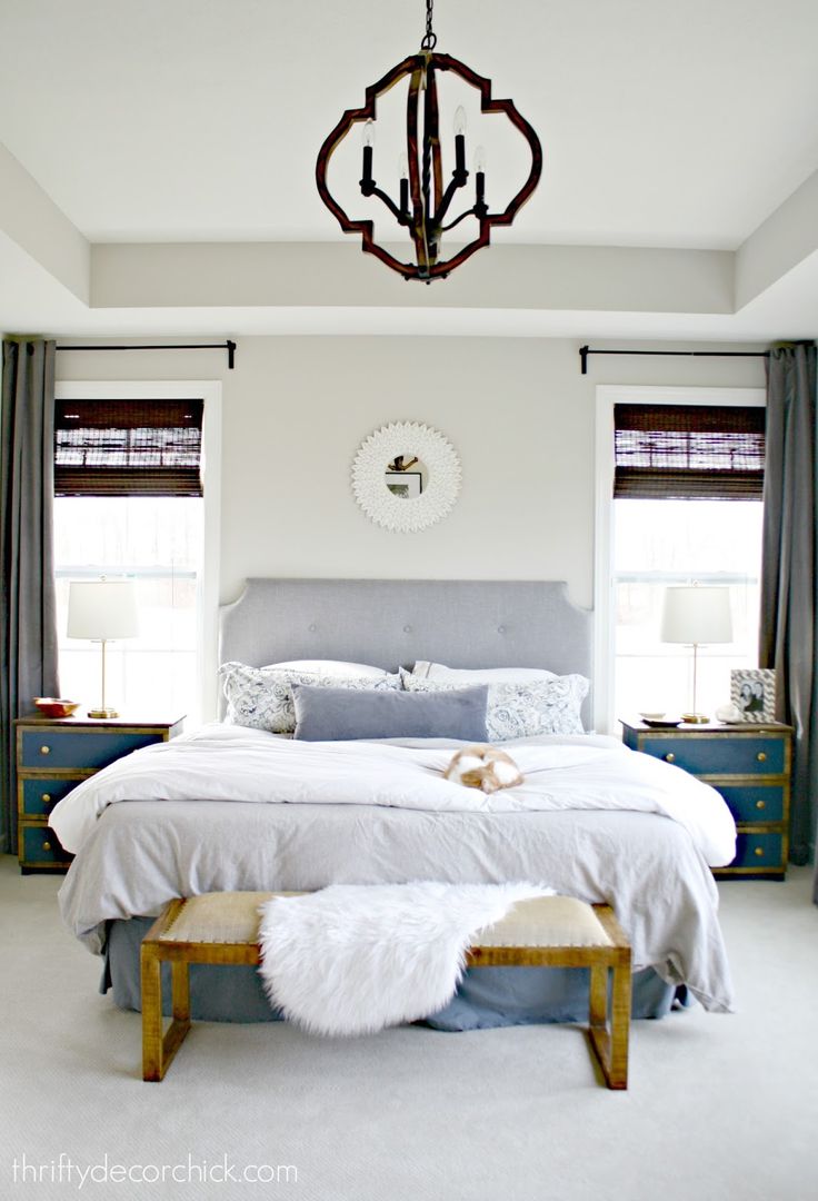 a bedroom with a bed, two windows and a chandelier hanging from the ceiling