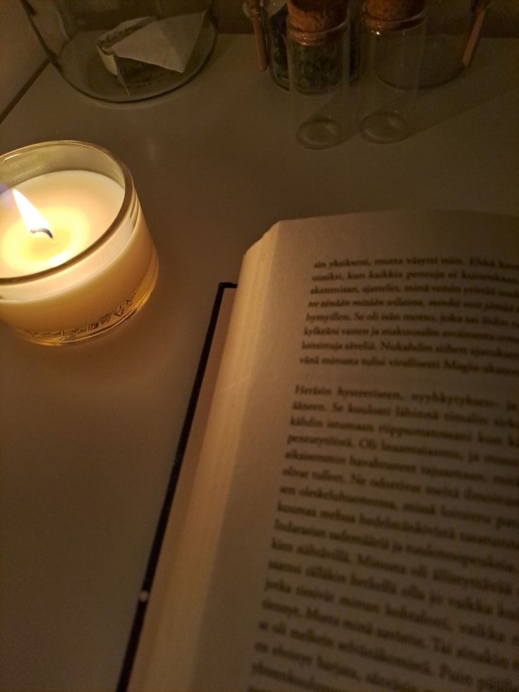 an open book sitting on top of a table next to a lit candle and jars