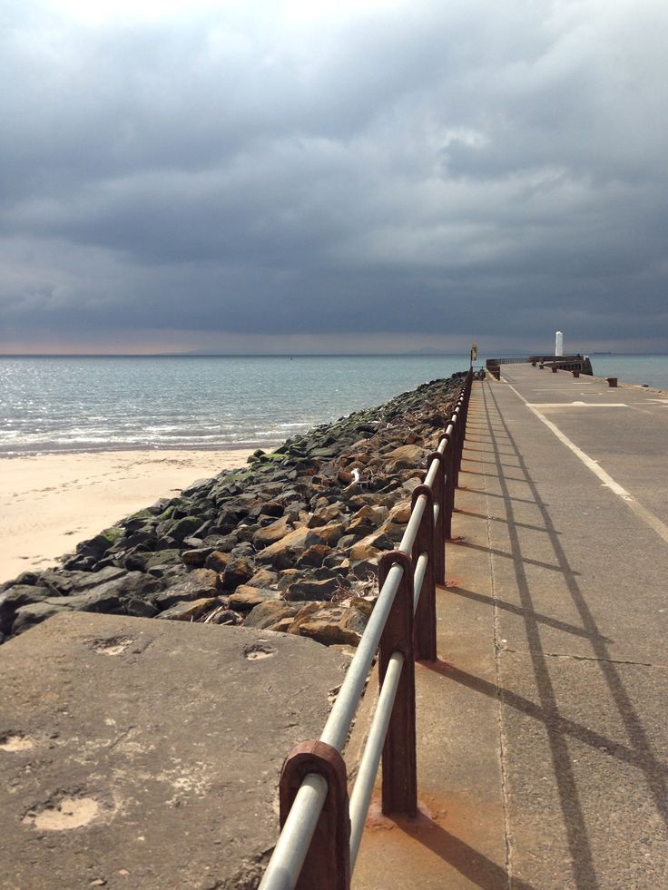 a long metal fence on the side of a road near the ocean under a cloudy sky