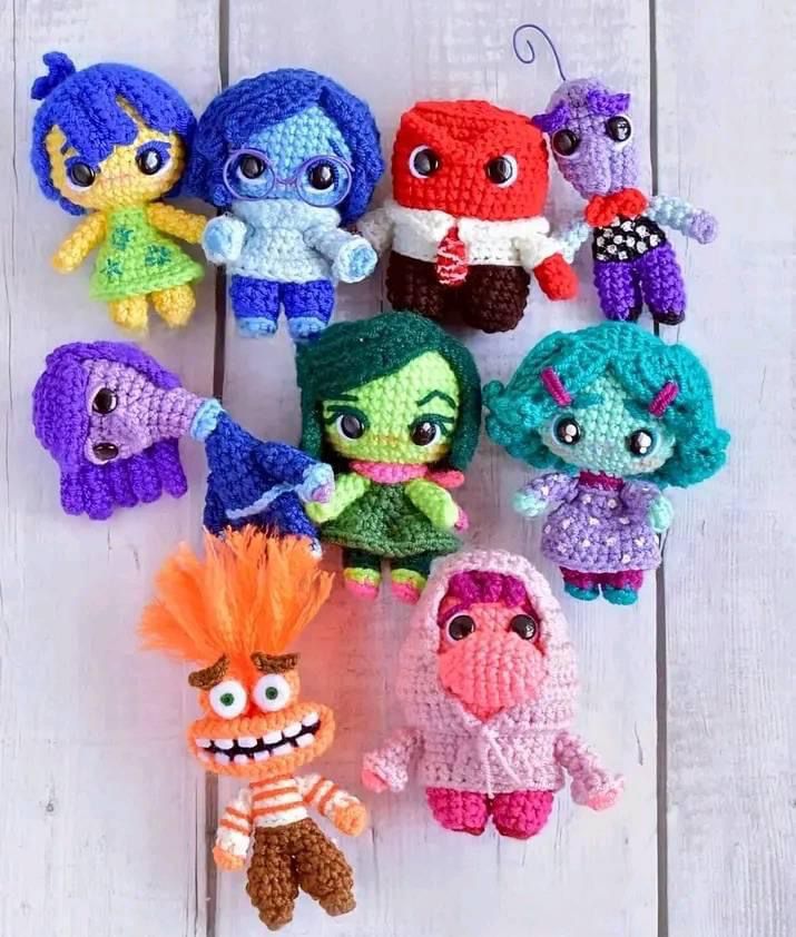 there are many small crocheted toys on the white wood floor, including one with an orange hair and two with blue eyes