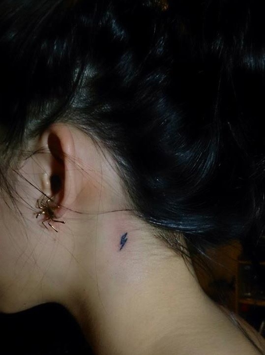 the back of a woman's neck with a tiny spider tattoo on her left ear