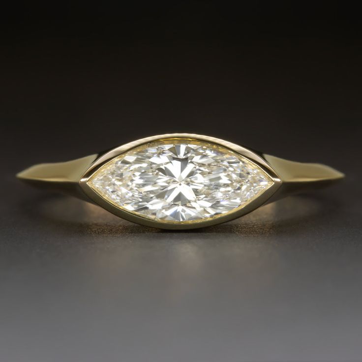 a yellow gold ring with a pear shaped diamond in the center on a black surface